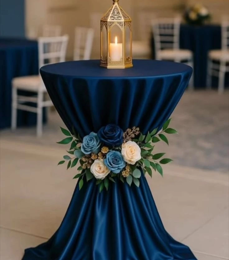 Mesa alta con mantel azul, arreglo floral y farol decorativo