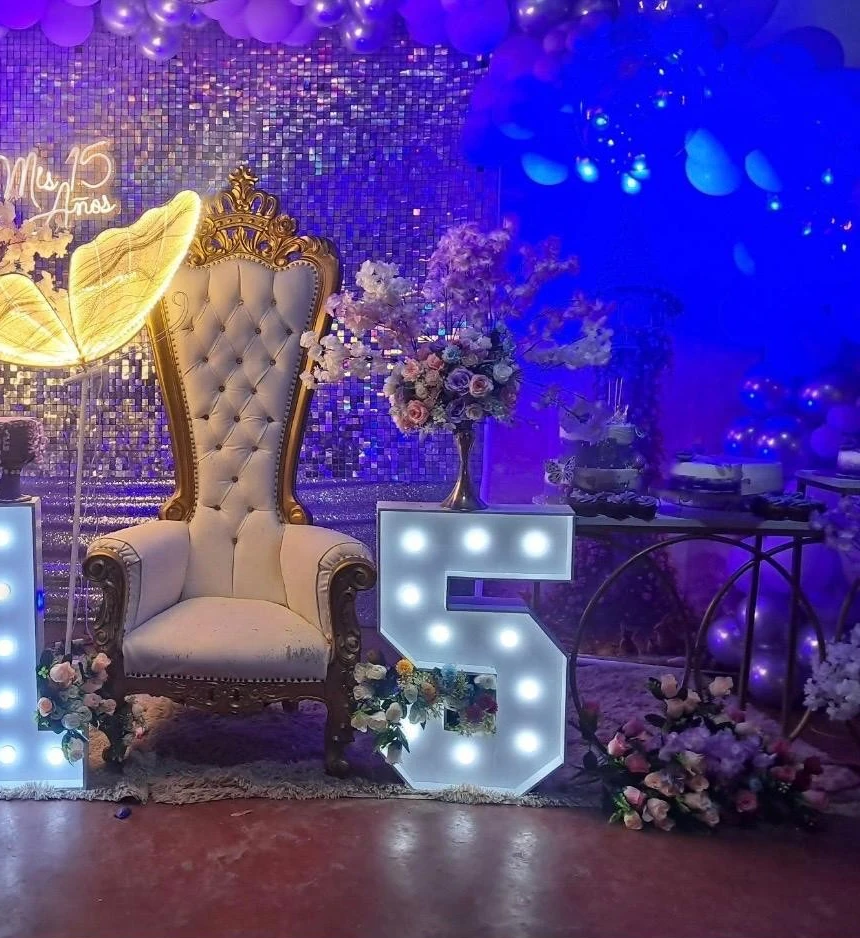 Escenario violeta de quince años con sillón, flores y números iluminados