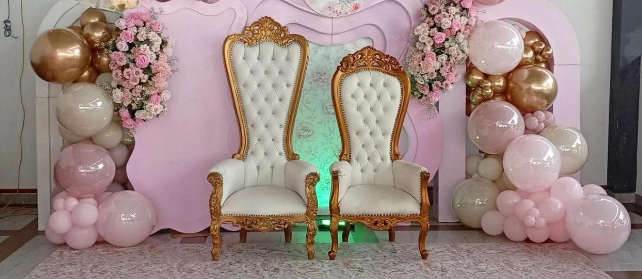 Dos sillones blancos y dorados frente a paneles rosados con globos y flores